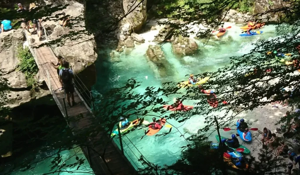 Defileul râului Soča din Slovenia, cu oameni care se bucură de activități de caiac pe apele sale de un verde smarald. Apele cristaline ale râului, împreună cu vegetația densă și podețele suspendate peste râu, subliniază frumusețea naturală și aventurile disponibile în această zonă. Râul Soča este bine cunoscut pentru oportunitățile sale de sporturi de apă, precum raftingul și caiacul, care atrag iubitorii de natură și de adrenalină din întreaga lume. Defileul râului Soča din Slovenia, cu oameni care se bucură de activități de caiac